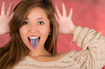 Woman with open mouth spreading tongue colored in blue with pink background and hand open with the fingers on her head