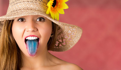Pink background with a beautiful girl using a nice hat with a sunflower, girl sticking out her blue...