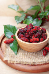 fresh organic mulberry in bowl on wooden background with mulberry fruit and mulberry branch. 