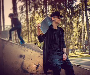 A man in black clothes posing with skateboard.