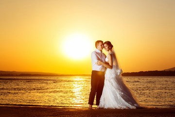 Fototapeta na wymiar Young man is embracing beautiful bride at amazing sea sunrise