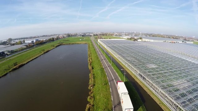Aerial of truck driving on road in the glasshouse greenhouse area showing a large greenhouse canal and a small lake and the road going straight in between the structures for growing plants 4k