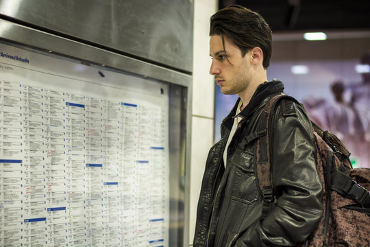 Young man traveling, reading train timetable in railway station