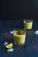 Delicious kiwi smoothie with mint and chocolate flakes, ice cubes and lime slices on wooden table. Healthy food.