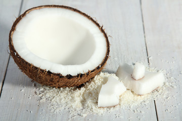 cut coconut with coconut flakes on white wood background