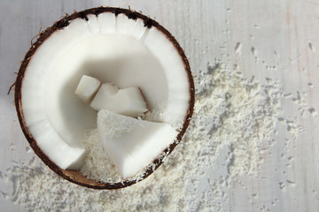 cut coconut with coconut flakes on white wood background