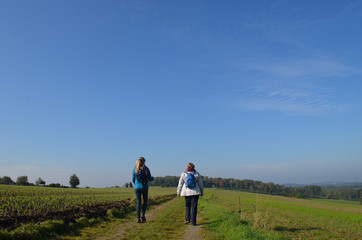 Fototapeta na wymiar Woman and girl walking on trail through rural landscape with meadows and fields on rolling hills in Wallonia on sunny autumn day, Durnal, Yvoir