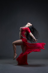 Young beautiful exotic eastern women performs belly dance in ethnic red dress on gray background