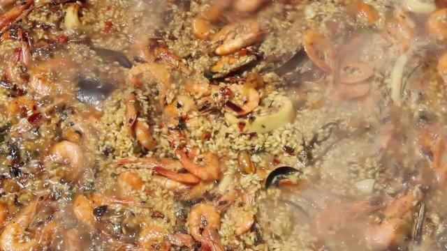 Removiendo con una espumadera la paella de marisco con caldo
( 2 Cortes )