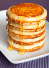 Pile of typical American pancakes with honey on white plate