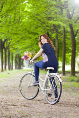 Fototapeta premium Beautiful young woman standing with a vintage bicycle at the par