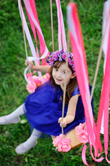 baby girl in a blue dress riding on a swing against the backdrop