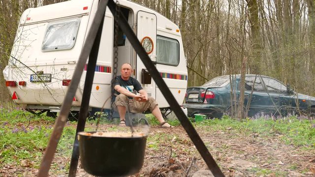 4K shot. Man Outdoors in caravan, trailer. Cooking up in wood campfire