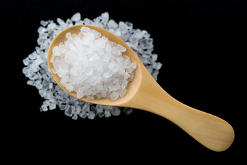 white crystals sea salt on wooden spoon on black background, top view
