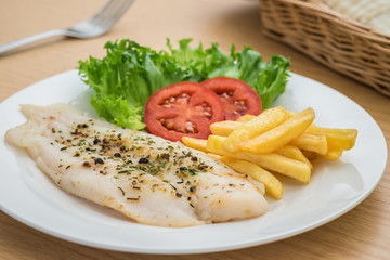 Grilled fish fillet steak with herb and french fries on plate
