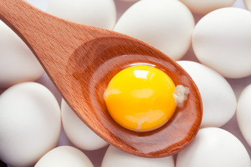 Egg yolk in wooden spoon on eggs - obrazy, fototapety, plakaty
