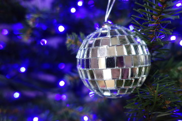 Silver ball hanging on a Christmas tree with blue lights in the background