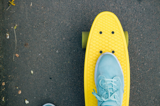 Female feet in blue sneakers on a yellow skateboard with green w