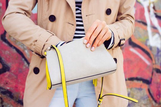 Woman in beige coat and jeans holding a lady's handbag on a back