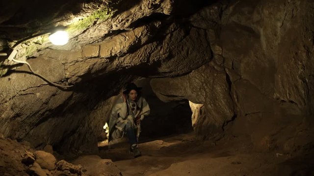 A young woman is standing inside a rock cave