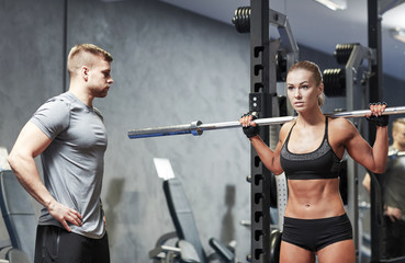 Fototapeta na wymiar man and woman with barbell flexing muscles in gym