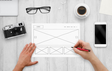 Web designer draw layout of website on paper. Top view of work desk with computer, phone, camera,...
