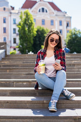 young woman with a limonade cup sitting on the stairs and text on her smartphone