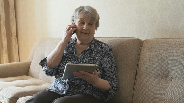 Old woman talking a mobile phone sitting on a sofa