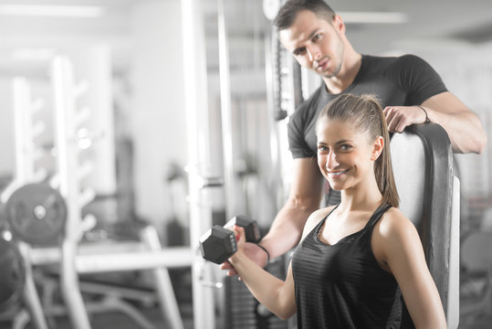 Woman Doing Bicep Curls In Gym With Her Personal Trainer