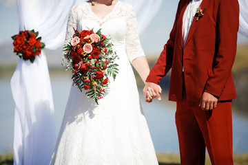 Wedding in style Marsala color. Bride and groom holding hands at altar.