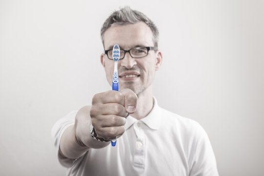Zahnarzt zeigt mit dem Zeigefinger auf eine blau weisse Zahnb&uuml;rste