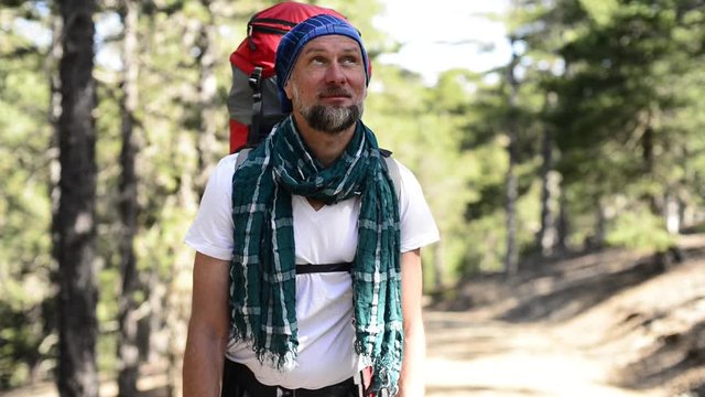 Bearded smiling hiker with a backpack standing on a mountain trail in the pine forest. Sunny day in Cyprus
