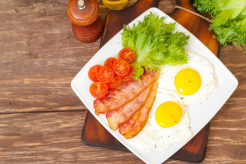 American Breakfast fried Eggs and bacon with tomato and lettuce on a wooden background 