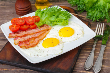 American Breakfast fried Eggs and bacon with tomato and lettuce on a wooden background 