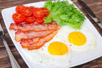 American Breakfast fried Eggs and bacon with tomato and lettuce on a wooden background 