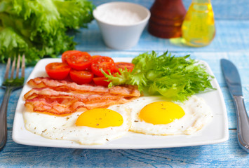American Breakfast fried Eggs and bacon with tomato and lettuce on a wooden background 