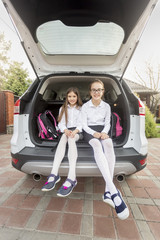 Two sisters ready to go to school sitting at car trunk