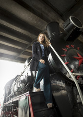 Beautiful young woman posing on big black steam locomotive
