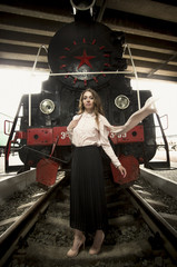 Elegant young woman standing on rails in front of old steam loco