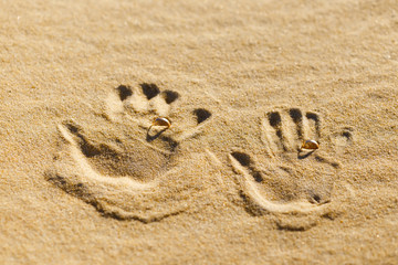 Two palm prints on the sand with wedding rings