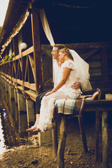 Toned photo of newly married bride and groom sitting on pier and