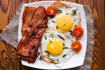 fried eggs with bacon and cherry tomatoes on a napkin on a wooden background