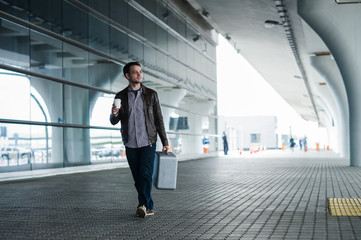 Fototapeta premium Full body portrait of a happy male traveler walking with bags and coffee