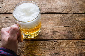 man holding a glass of beer on a wooden background