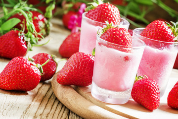 Pink granita with strawberries in a glass, old wooden background