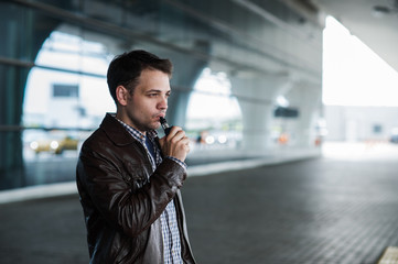 Urban lifestyle portrait of a man vaping near the airport before registration with custom vape mod...