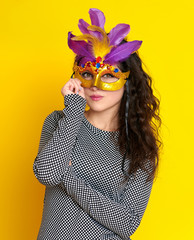 woman in carnival masquerade mask with feather, beautiful girl portrait on yellow color background, long curly hair