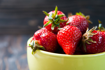 strawberry fruit in yellow pottery cup on dark wooden background