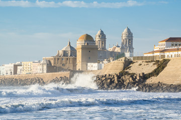 View of the Ancient Cadiz Cathedral. The waves on the winter Atlantic Ocean. Spain - obrazy, fototapety, plakaty
