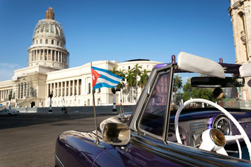 Cuban flag on a classic car with the Capitolio on the background in Havana, Cuba